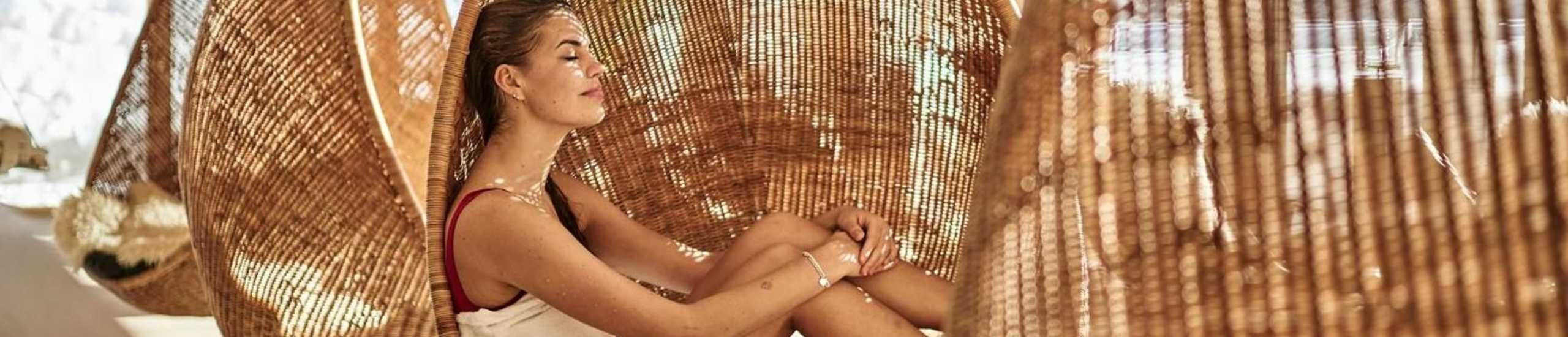 Frau sitzt bei strahlenden Sonnenschein gemütlich in einem Hängesessel im Wellnessbereich